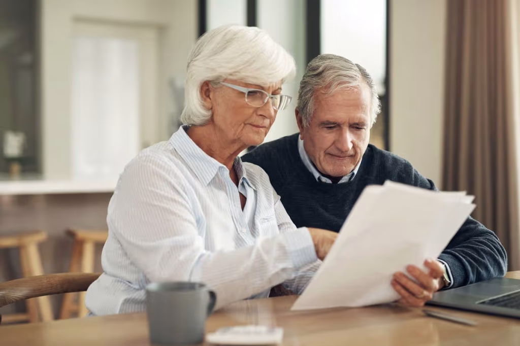 Retired couple examining pension documents while discussing household finances.